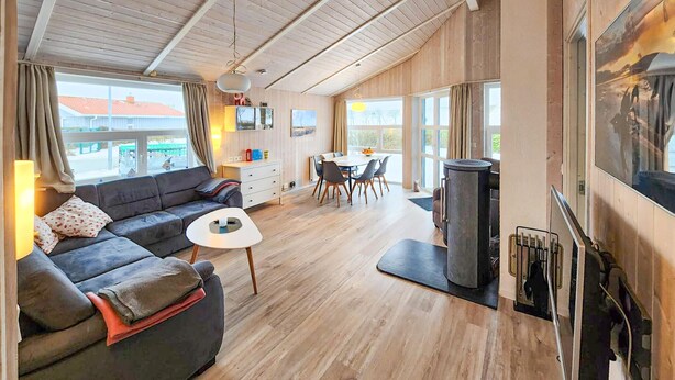 En hyggelig stue med sofa, et lille bord, et spiseområde med stole, pejs og store vinduer.