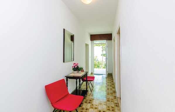 A hallway with a red chair, a small table with a potted plant, and a door leading outside.