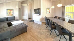 A modern living room with a grey sectional sofa, a white coffee table, and a dining area with a long wooden table and black chairs. - Friedrichskoog-Strandpark 3 (Friedrichskoog)