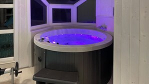 A corner hot tub with a built-in seat and a control panel, surrounded by wooden walls and a window. - Friedrichskoog-Strandpark 3 (Friedrichskoog)