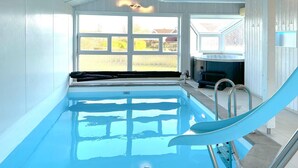 A swimming pool with a slide, a hot tub, and a view of the outdoors through large windows. - Friedrichskoog-Strandpark 3 (Friedrichskoog)