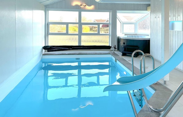 A swimming pool with a slide, a hot tub, and a view of the outdoors through large windows.