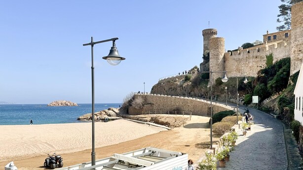Un sentier côtier qui longe un château, une plage et un quai pour bateaux.