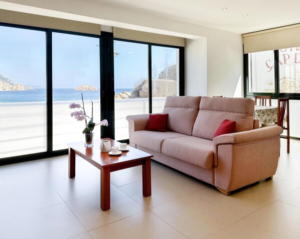 A modern living room with a beige sofa, a wooden coffee table, and a view of the sea through large windows. - AMAZING APARTMENT SEA VIEWS IN TOSSA (Tossa de Mar)