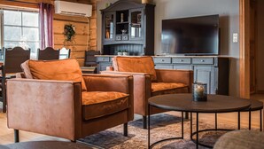 A cozy living room with leather armchairs, a round coffee table, a flat-screen TV, and a wooden cabinet. - 10 bedroom amazing home in ølen (Ølen)