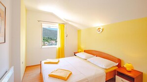 Een hotelkamer met een bed, een nachtkastje, een lamp, een raam met uitzicht op een berg en bomen, en een geel gordijn.