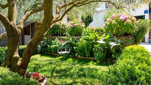 Een weelderige tuin met verschillende planten en bloemen, een stenen muur en een gebouw op de achtergrond.