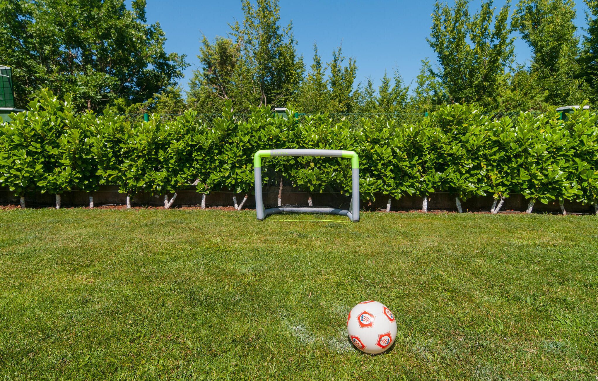 A soccer goal on a grassy field with a soccer ball in front of it.