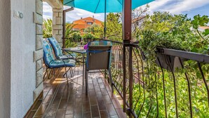 A balcony with two chairs and a table, a blue umbrella, and a view of a garden and buildings. - 2 bedroom gorgeous apartment in Medulin (Medulin)