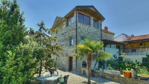 A stone building with a balcony, outdoor seating, and a palm tree.