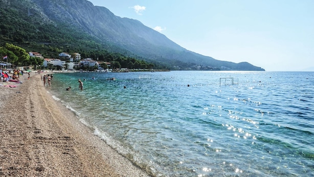 A beach with clear shallow waters, a pebbly shore, and a mountainous backdrop. - Pet friendly apartment in Zivogosce (Zivogosce)