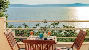 A balcony with a table set for two, overlooking a body of water and distant mountains. - Pet friendly apartment in Zivogosce (Zivogosce)