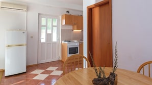 A compact kitchen with a refrigerator, oven, and a dining area with a table and chairs. - Pet friendly apartment in Zivogosce (Zivogosce)