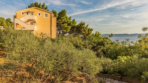 A modern two-story building with a flat roof, surrounded by dense greenery and overlooking a body of water. - Pet friendly apartment in Zivogosce (Zivogosce)