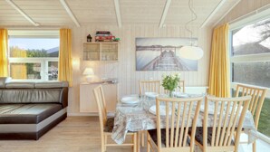 A cozy dining area with a wooden table set for four, surrounded by wooden chairs. A sofa is positioned against the wall, and a large window offers a view of the outdoors.