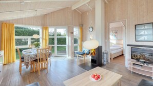 A spacious room with a wooden ceiling, a dining area with a table and chairs, a sofa, a fireplace, and a television.