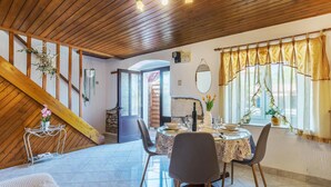 Zona pranzo con soffitto in legno, parete in pietra e finestra con tende.