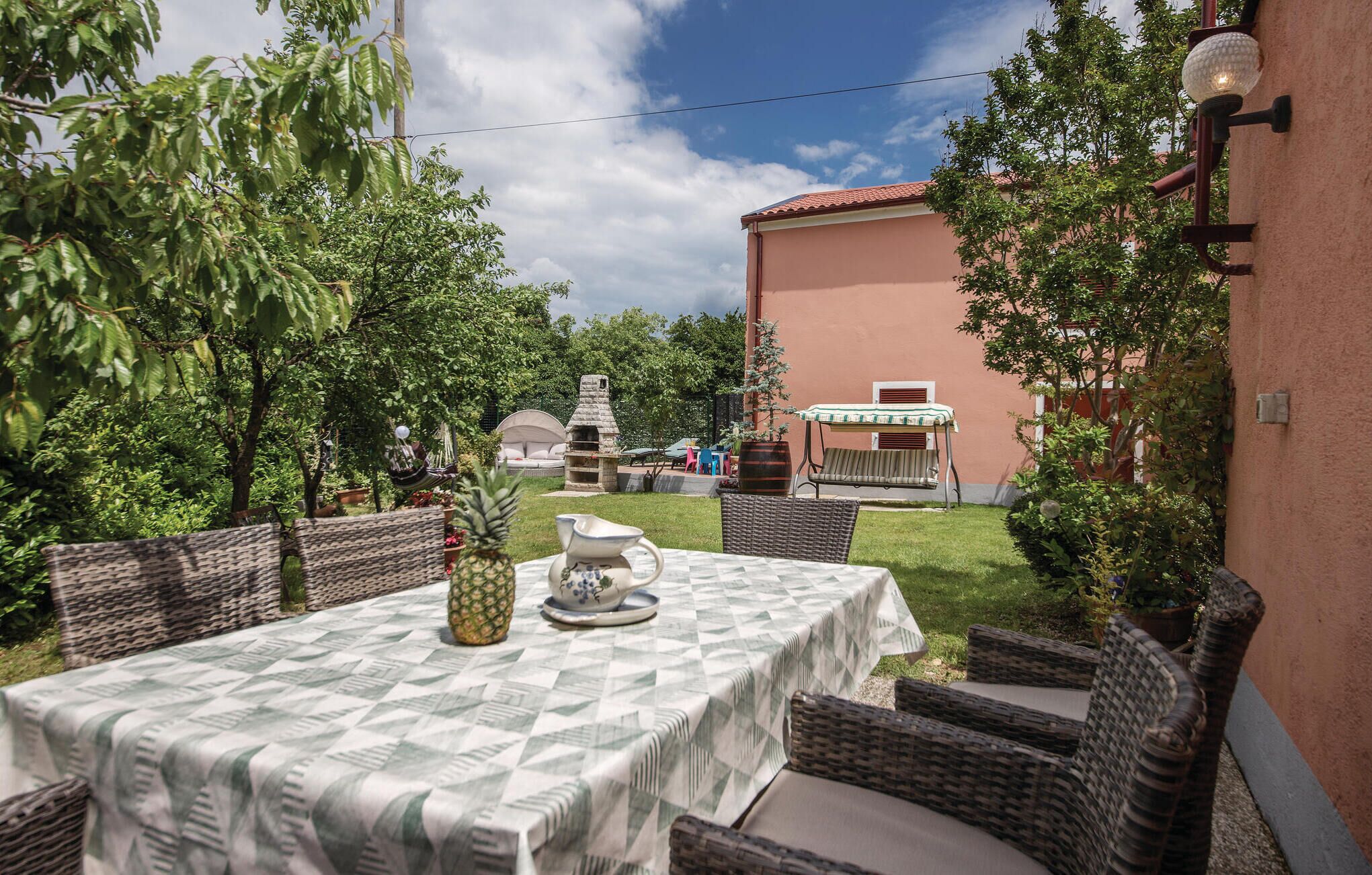 En udendørs terrasse med fletningsmøbler, et bord med et mønstret borddække, en ananas og en kande.