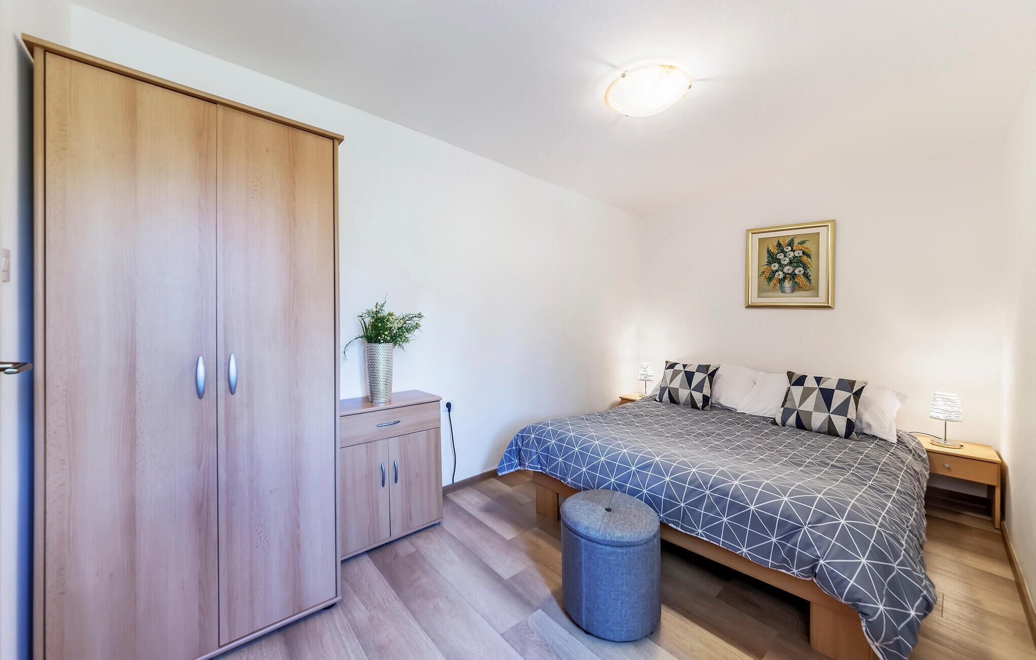 A bedroom with a bed, a wardrobe, a bedside table, a lamp, and a framed picture on the wall.