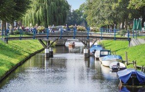 Een gracht met aan de rechterkant stilgelegde boten, een voetgangersbrug op de achtergrond en een menigte mensen aan de linkerkant.