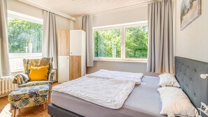 Quarto com cama, cadeira, guarda-roupa e janelas amplas.