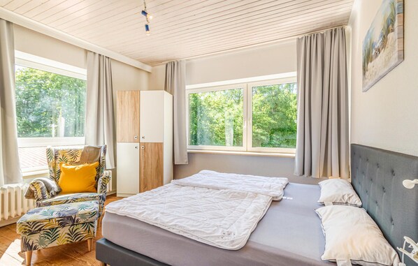 Een slaapkamer met een bed, een stoel, een kledingkast en grote ramen.