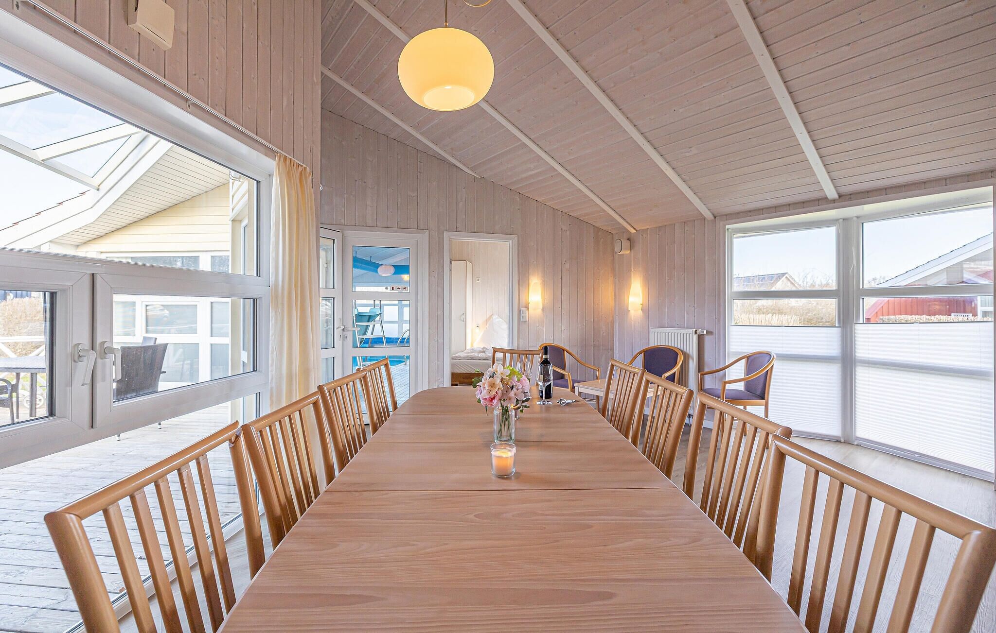 A long wooden table with chairs, a vase with flowers, and a bottle of wine in the center.