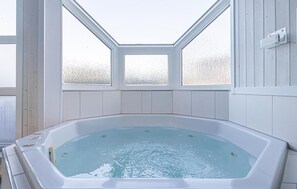 Un jacuzzi con tragaluz, paredes blancas y vistas a árboles.