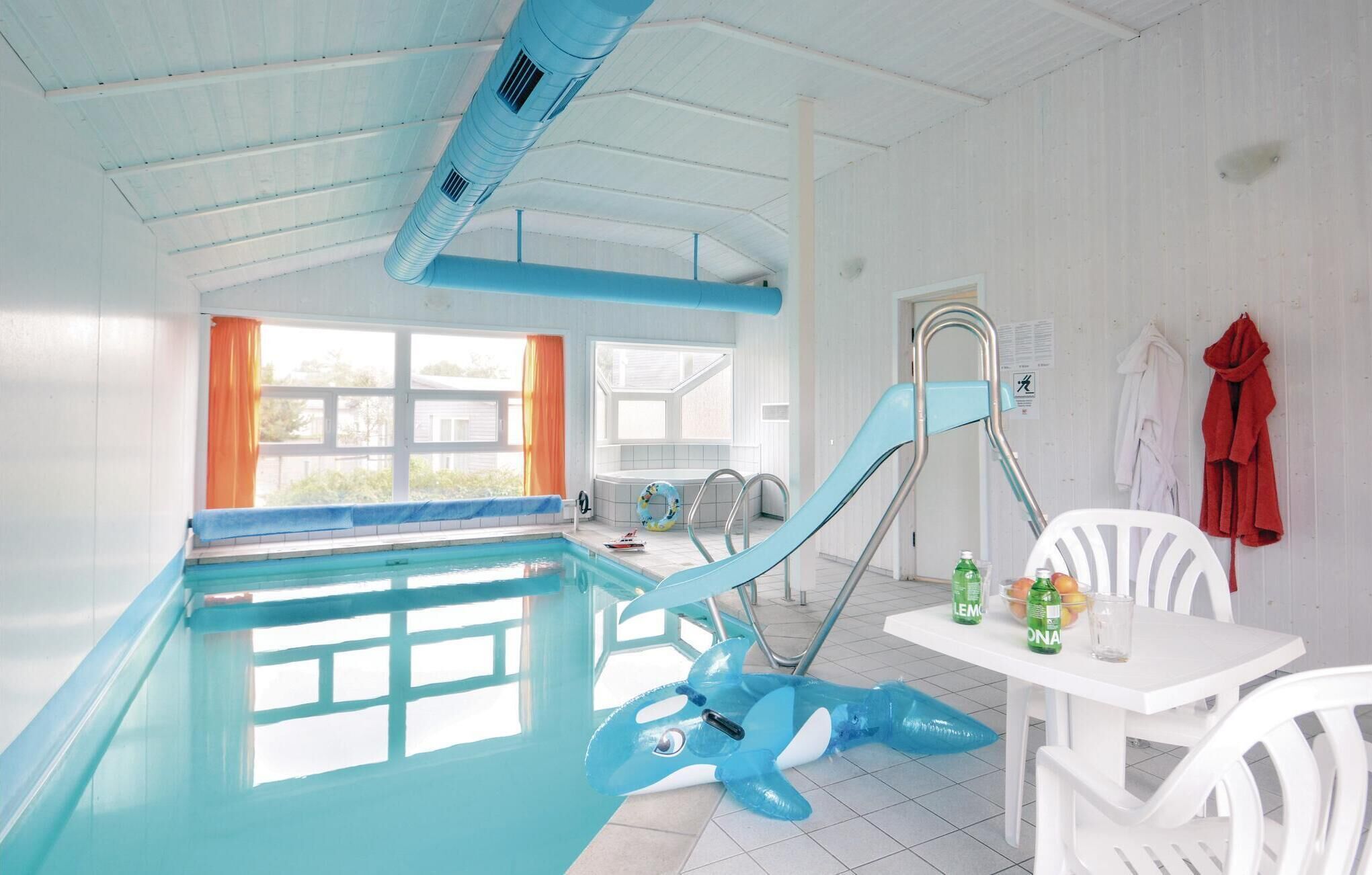 Ein Hallenbad mit einem blauen aufblasbaren Hai, einem weißen Tisch mit Getränken und einem Fenster mit orangefarbenen Vorhängen.