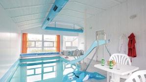 Ein Hallenbad mit einem blauen aufblasbaren Hai, einem weißen Tisch mit Getränken und einem Fenster mit orangefarbenen Vorhängen.