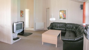 Ein Wohnzimmer mit einer schwarzen Ledersofa, einem Holztisch, einem Fernseher auf einem Schrank und zwei Bildern an der Wand.