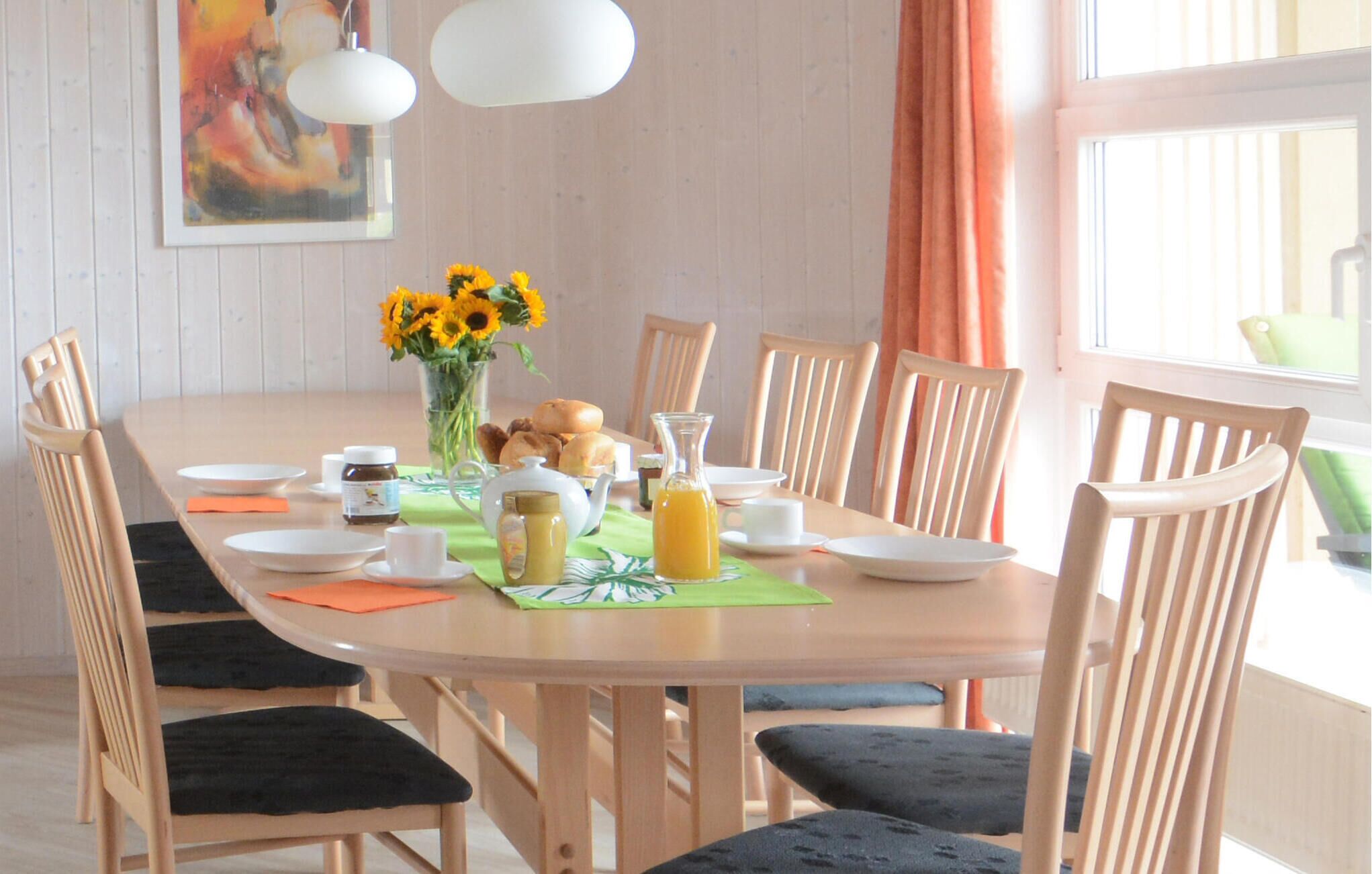 Mesa lista para el desayuno con sillas, un jarrón de girasoles y diferentes alimentos para el desayuno.