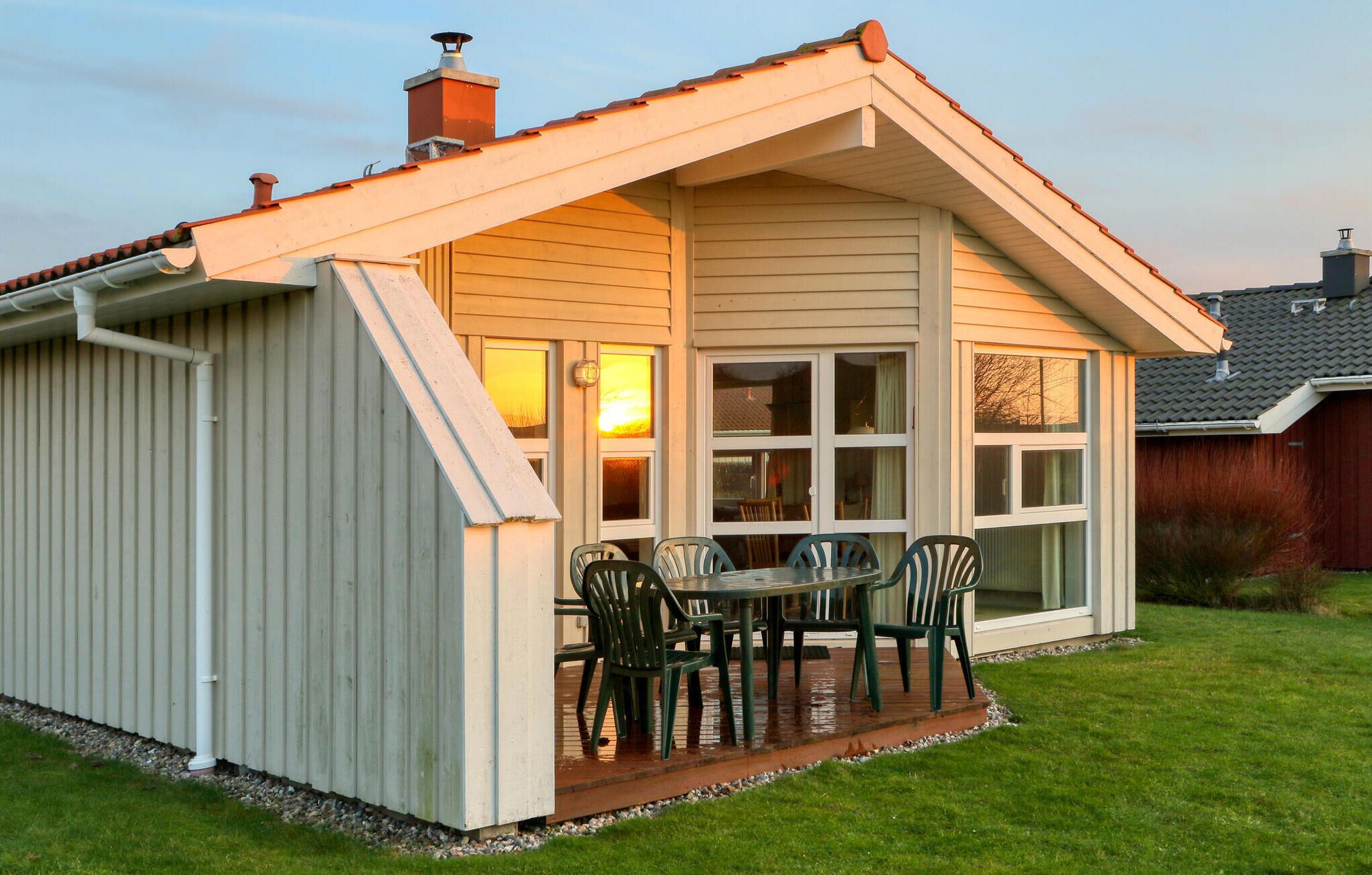 A small, single-story house with a sloped roof, a porch with a table and chairs, and a window with a view of the sunset.