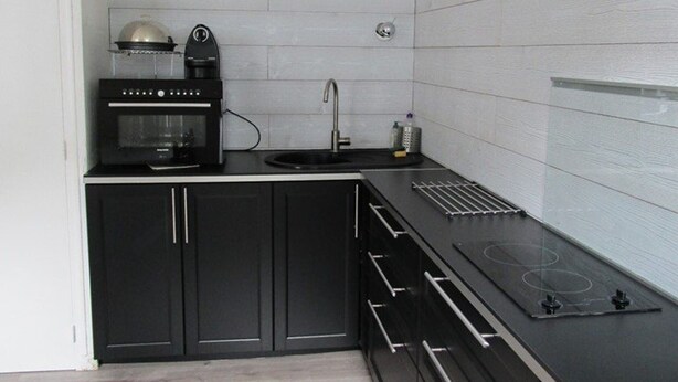 A modern kitchen with black cabinets, a built-in oven, a coffee maker, and a sink.