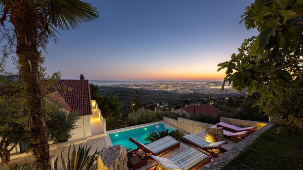A poolside area with lounge chairs and a view of a cityscape at dusk.