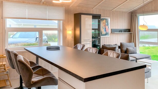 A modern kitchen with a central island, bar stools, and a dining area with a sofa. - Friedrichskoog-Strandpark 15 (Friedrichskoog)