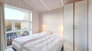 A bedroom with a large window, a bed, a wardrobe, and a small table with chairs. - Friedrichskoog-Strandpark 15 (Friedrichskoog)