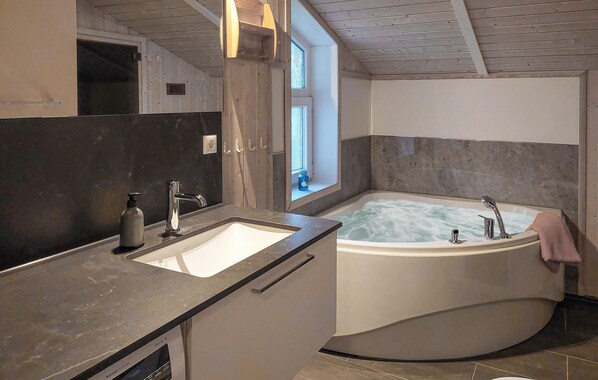 A modern bathroom with a large bathtub, a sink, and a window providing natural light. - Gorgeous home in Schönhagen with sauna (Schönhagen)