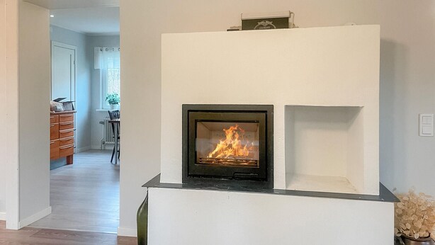 Ein moderner Kamin mit sichtbarem Feuer, eine weiße Wand und ein Holzboden.