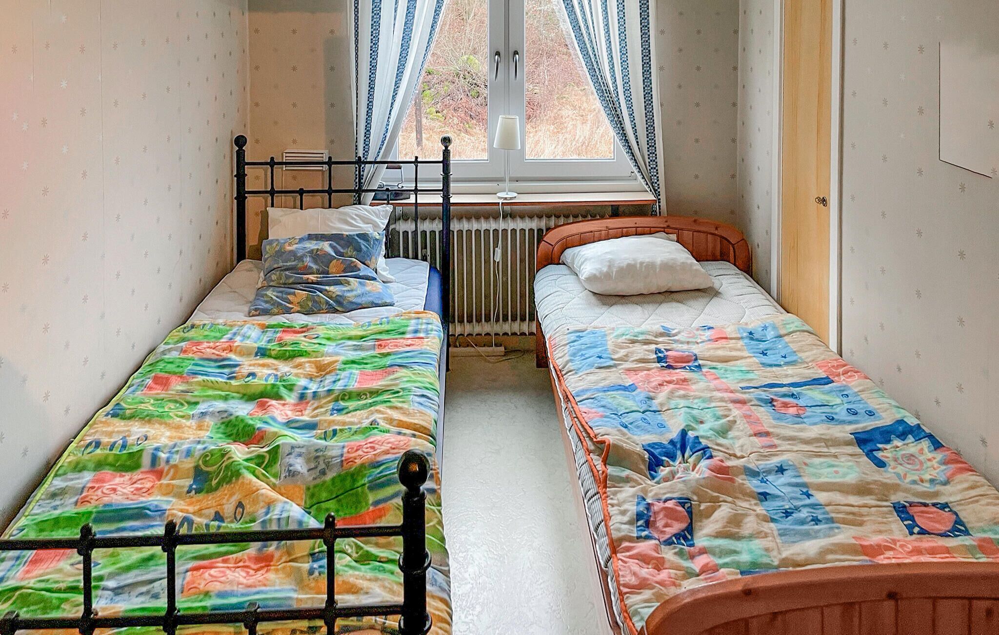 Une petite chambre agréable, dotée de deux lits simples, d’un radiateur, d’une fenêtre avec des rideaux et d’un cache-radiateur.