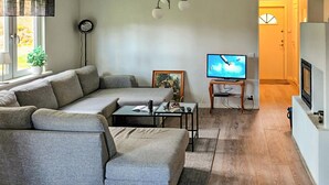 Ein Wohnzimmer mit einem grauen Ecksofa, einem kleinen Couchtisch, einem Fernseher auf einem Schrank und einer Tür, die in einen anderen Raum führt.