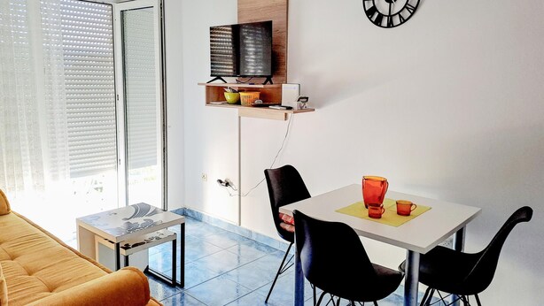 A compact living space with a dining area, a sofa, a TV on a shelf, and a clock on the wall. - 1 bedroom lovely apartment in Klek (Klek)