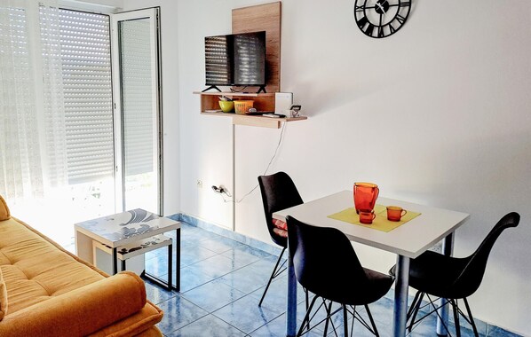 A compact living space with a dining area, a sofa, a TV on a shelf, and a clock on the wall.