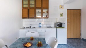A compact kitchen with wooden cabinets, a microwave, a kettle, and a small refrigerator. - 1 bedroom lovely apartment in Klek (Klek)