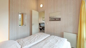 Un dormitorio con cama, una puerta, un radiador y una ventana con cortinas.