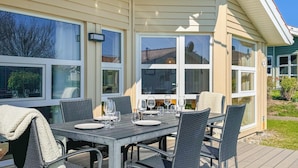 Un espace extérieur aménagé pour les repas, avec une table dressée pour quatre personnes, entourée de chaises en osier.