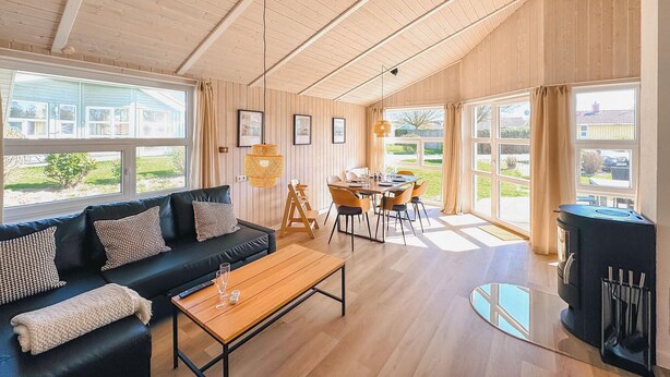 Un vaste espace de vie doté d’un plafond en bois, d’un canapé noir, d’une table basse en bois et d’une table à manger avec des chaises.