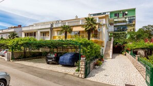 A residential building with a covered carport, stone pathway, and a green fence.