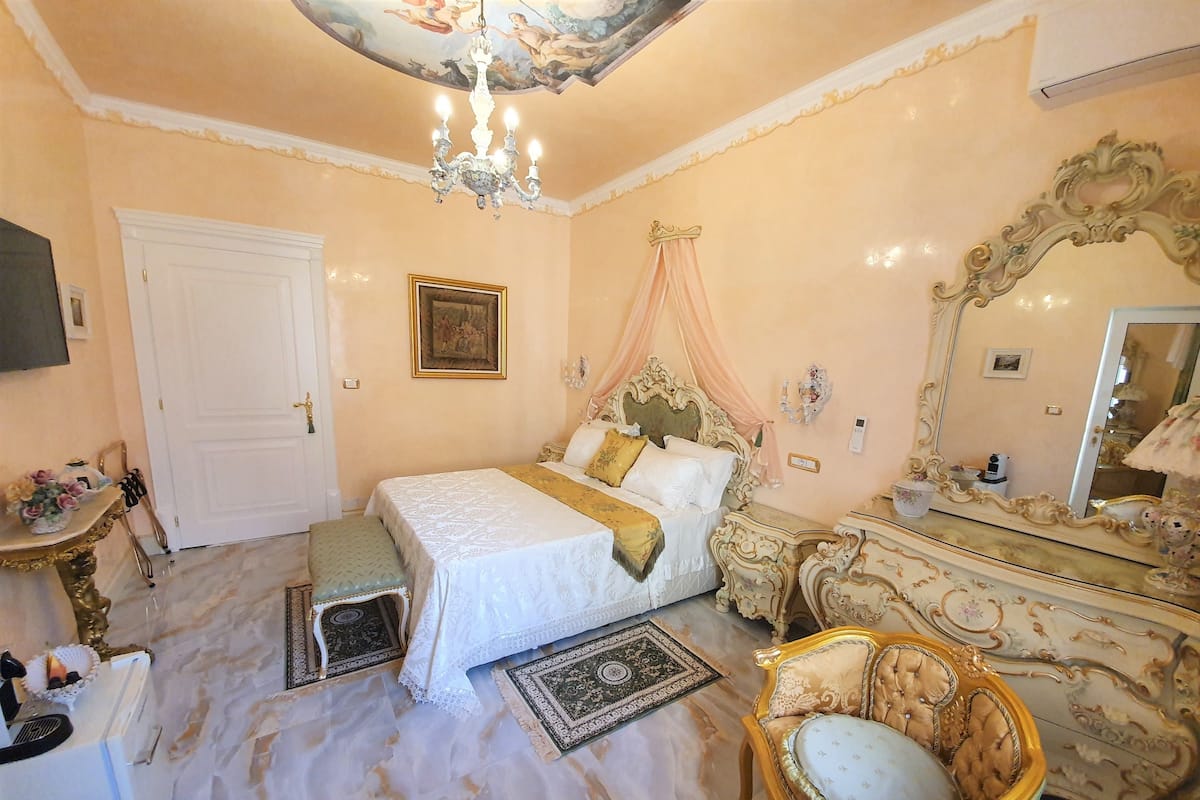 Quarto com uma cama grande, toucador com espelho, candelabro e teto decorativo.