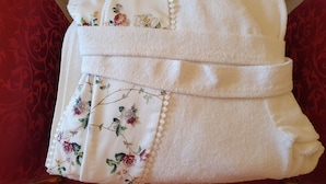 A neatly folded white towel with floral embroidery and pearl accents, placed on a red upholstered chair. - FD Luxury Rooms (Verona)